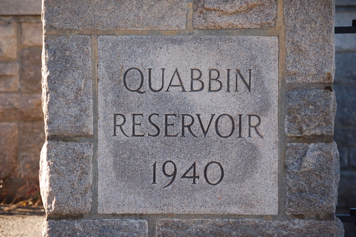 A carved stone sign reading Quabbin Reservoir beside a lawn and trees